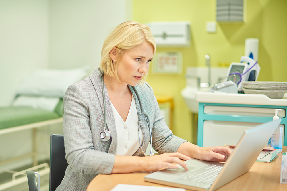 Image of a doctor in an exam room typing on a laptop